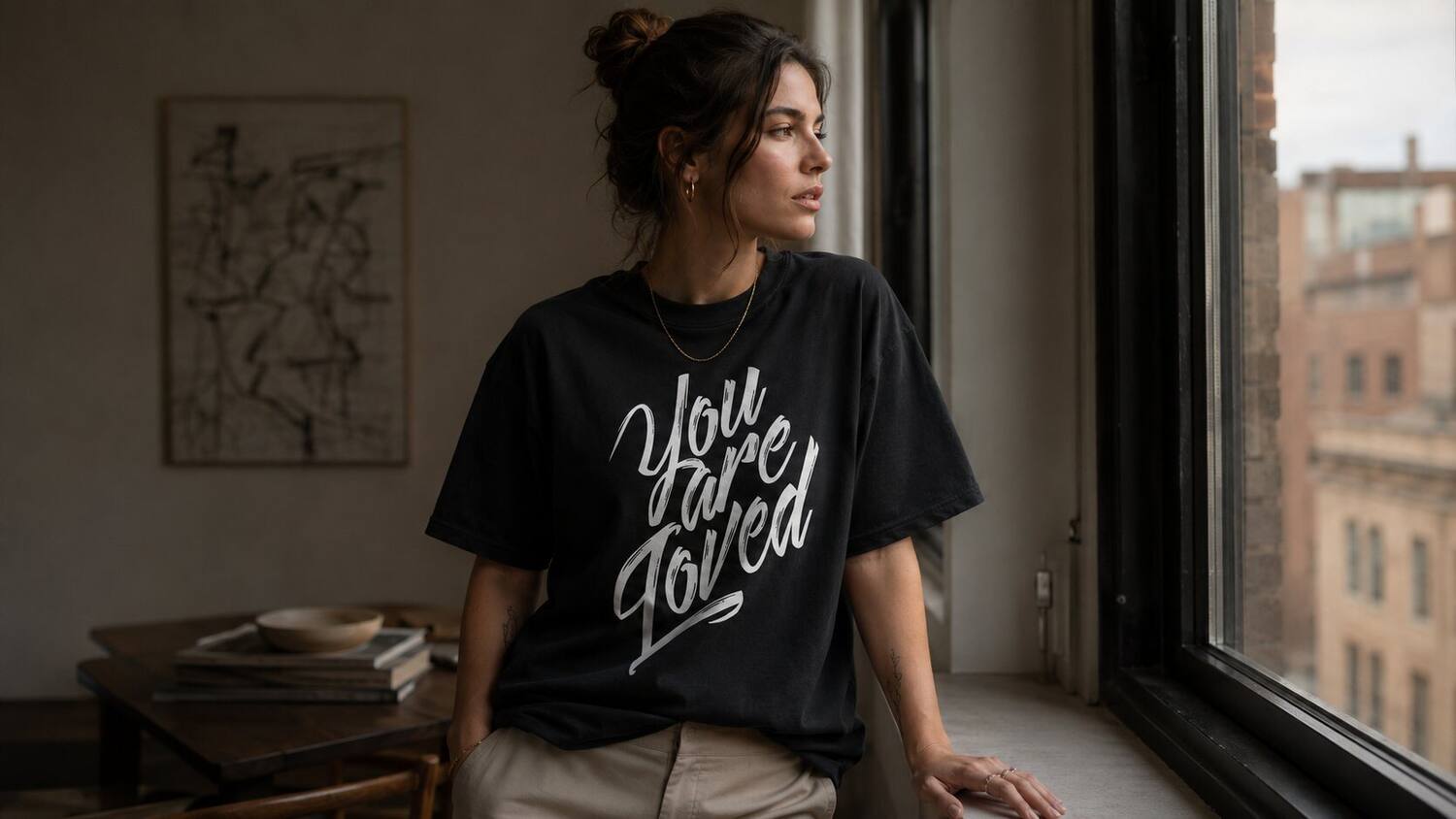 A woman in a You Are Loved tee by a window